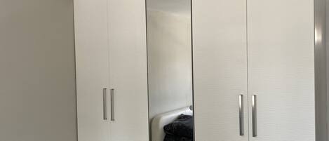 Ein modernes Schlafzimmer mit großem Kleiderschrank, einem Bett und einer Deckenleuchte.