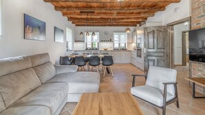 A modern living room with a wooden ceiling, a dining area with a kitchen in the background, and a TV mounted on the wall. - Gorgeous home in Cabrunici (Cabrunici)