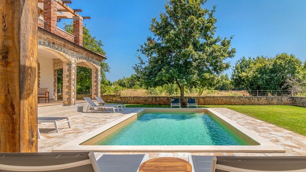 A swimming pool with lounge chairs and a wooden table, surrounded by stone walls and greenery. - Gorgeous home in Cabrunici (Cabrunici)