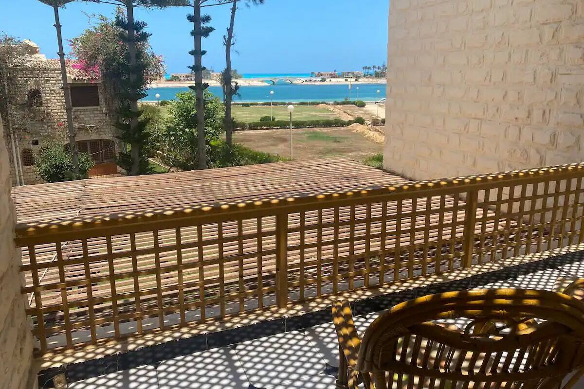 A balcony with a view of the sea, a wooden fence, and a wicker chair.