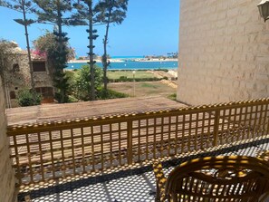 A balcony with a view of the sea, a wooden fence, and a wicker chair. - Sunny 4-Bedroom Townhouse Families Only (Al-Hammam)