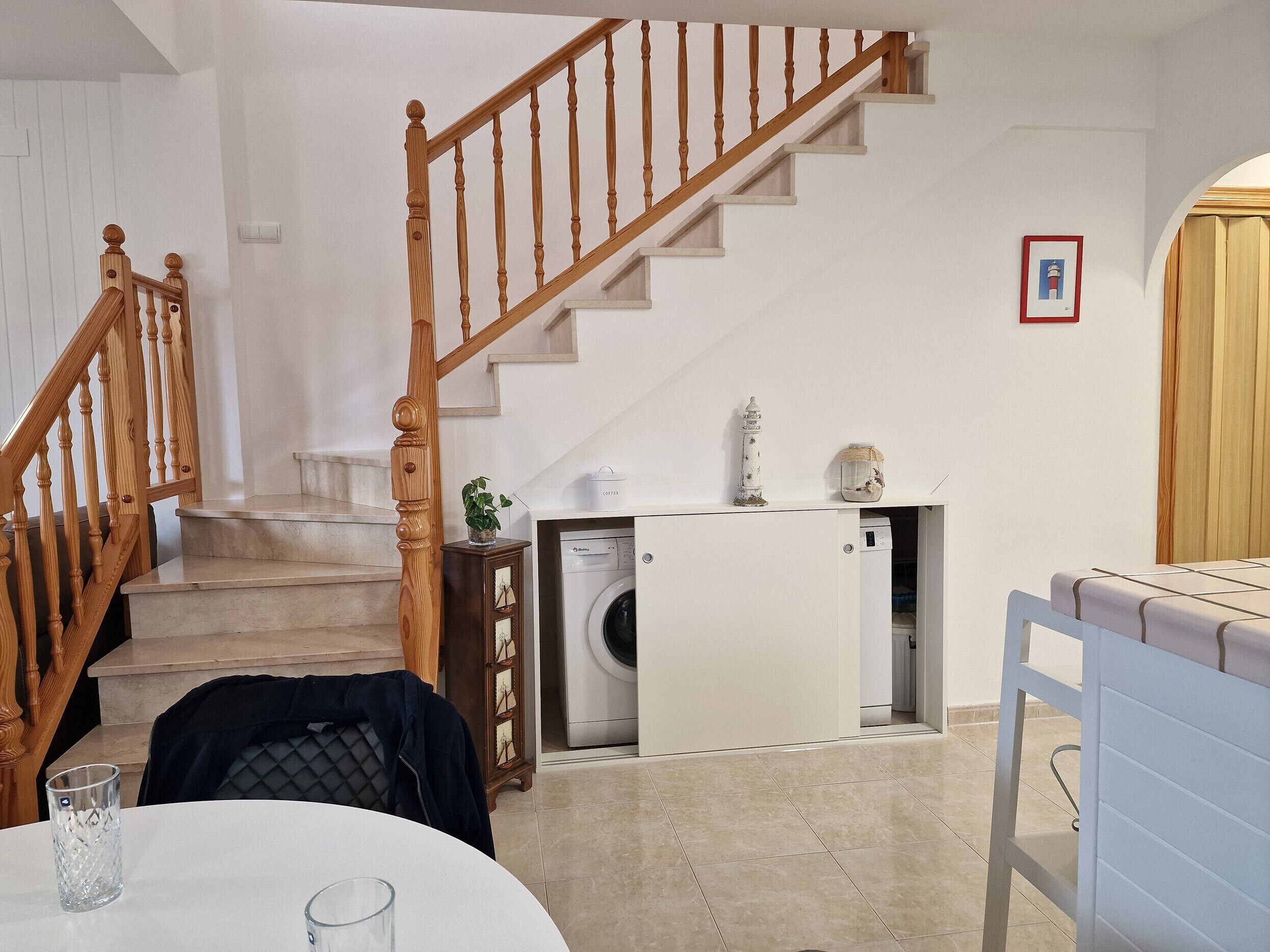 A staircase with wooden balusters, a washing machine, and a small cabinet with a plant.