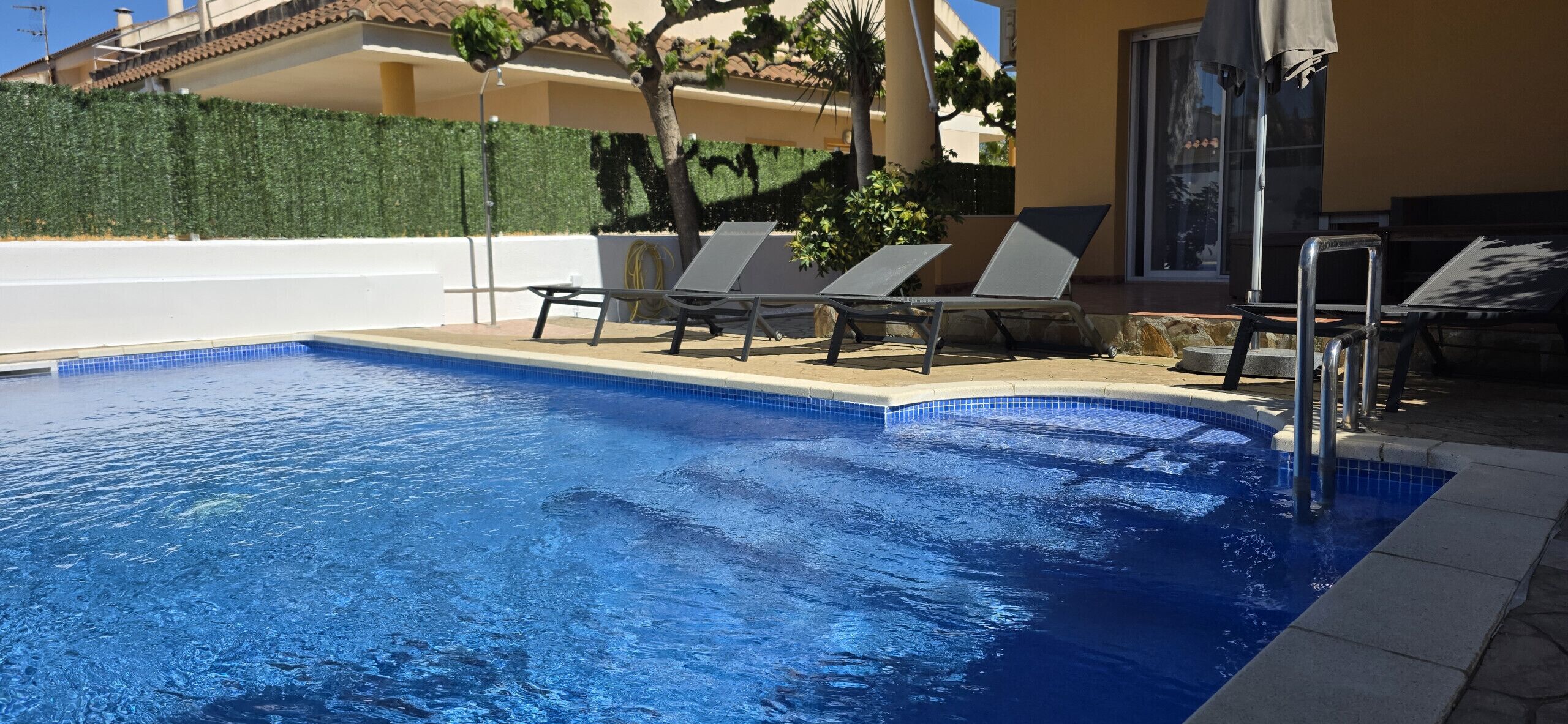 A swimming pool with lounge chairs and a glass door entrance.