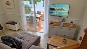 A living room with a sofa, a wooden table, a TV, and a view of an outdoor patio. - "Gecko"@MARISOL: 250m to the beach, private pool, A/C, WiFi, dog beach (Riumar)