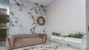 A modern lobby with a marble wall, a brown cushioned sofa, a white console table with plants, and a circular wooden decor piece. - Doki Studio Stocznia by Grand Apartments (Gdansk)