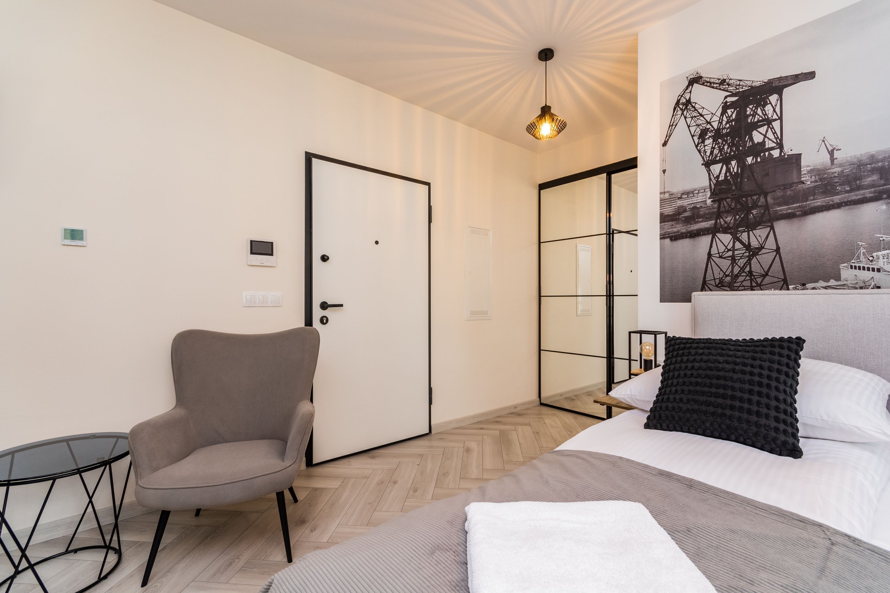 Ett hotellrum med en säng, en stol, ett litet bord, en dörr och en väggmonterad lampa.