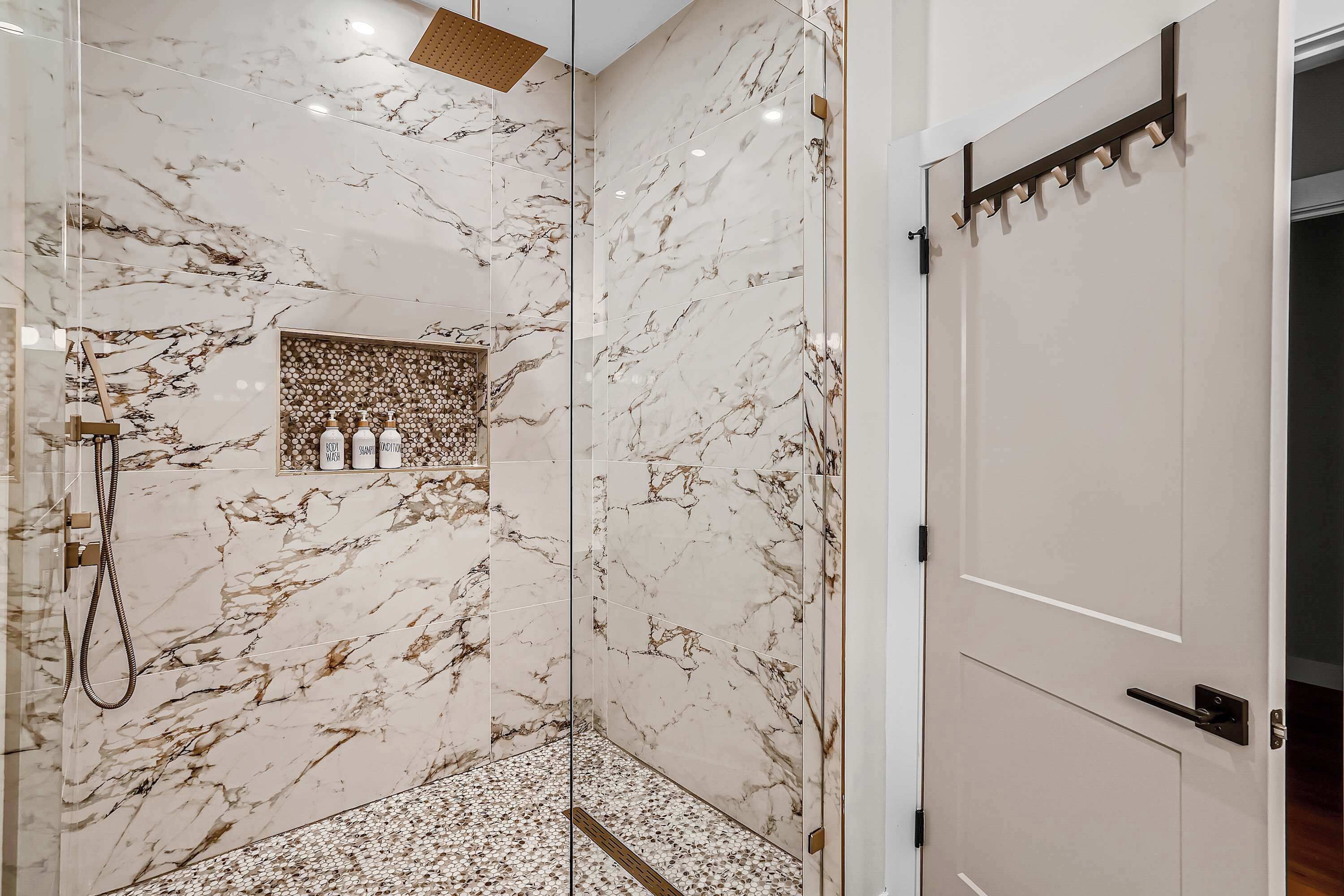 A modern bathroom with marble walls, a shower, and a door with a coat rack.