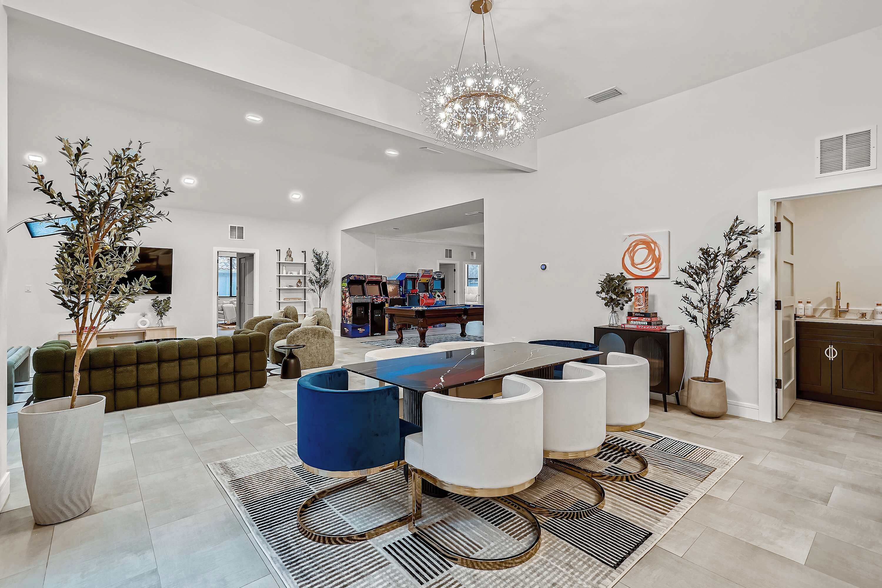 A modern living room with a large dining table, sofas, and potted plants.