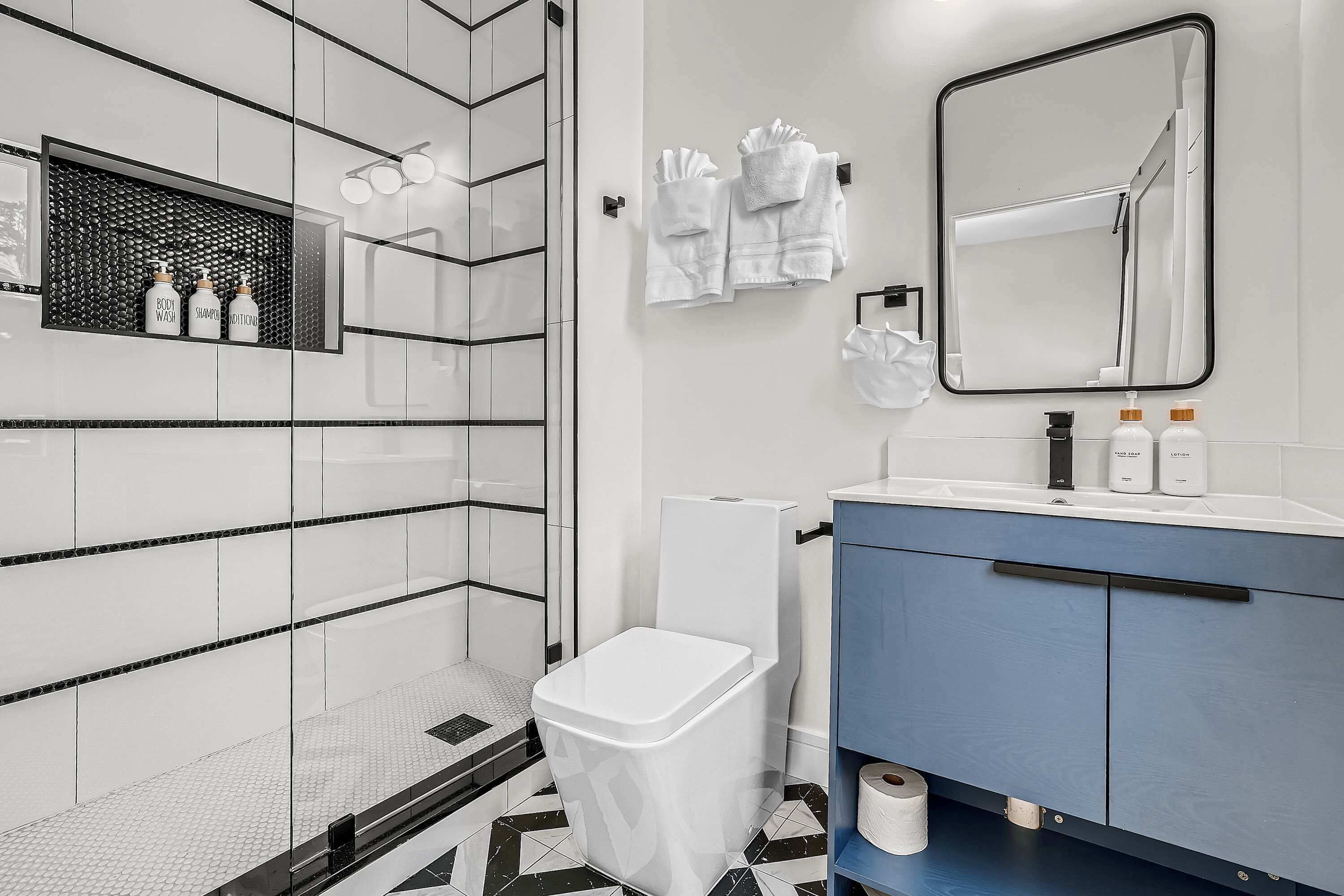 Un baño moderno con suelo de baldosas blancas y negras, un tocador azul, un inodoro blanco y un espejo sobre el lavabo.