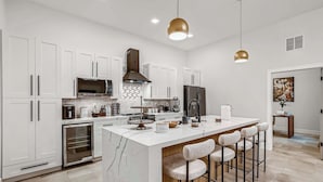 A modern kitchen with white cabinetry, a central island with bar stools, stainless steel appliances, and pendant lighting.