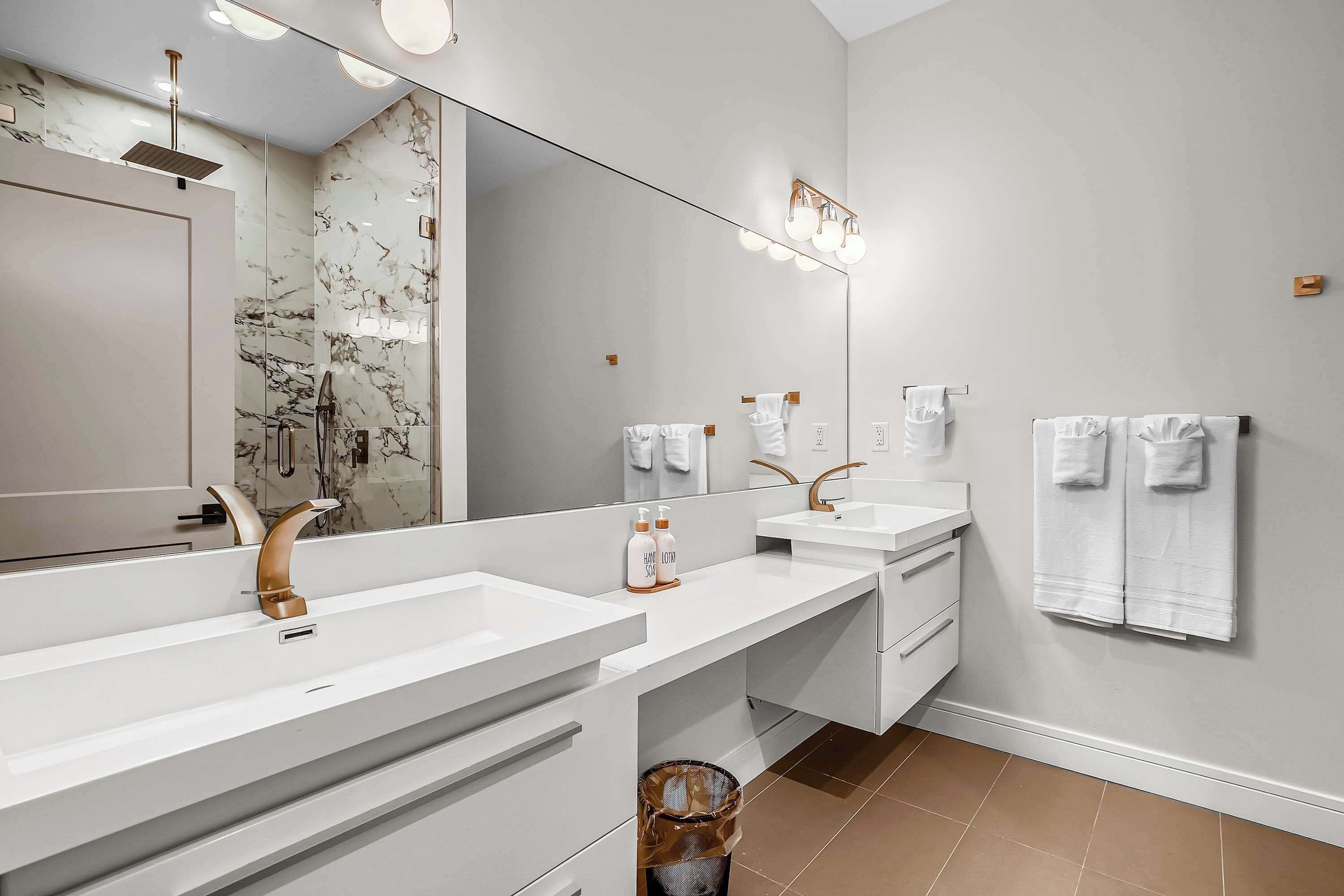 A modern bathroom with two sinks, a large mirror, and a trash bin.