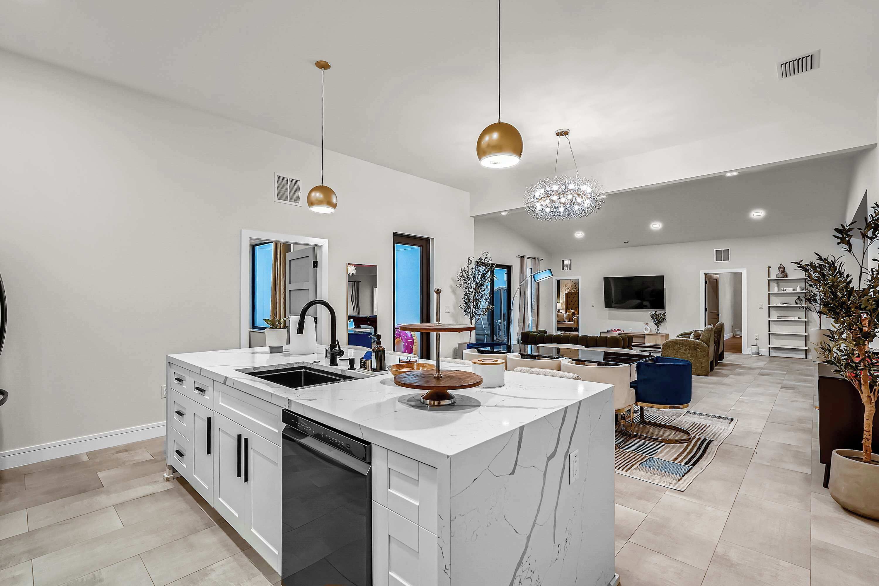 A spacious kitchen with a large island, modern pendant lights, and a central chandelier.