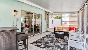 Ein überdachter Patio-Bereich mit Korbmöbeln, einer Couch und einem Esstisch.