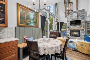 Enjoy meals in the dining area with a round table and four chairs, surrounded by a beautiful framed painting and a cozy seating area with a sofa and fireplace.