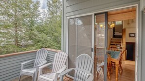 Eine Terrasse mit Adirondack-Stühlen und einer Glastür zu einem Essbereich mit Tisch und Stühlen.