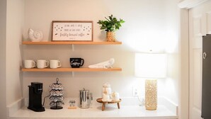 Een keukenblad met een koffiezetapparaat, mokken, een bord met koffie-thema en een decoratieve plant.