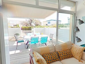 A room with a sofa, a table, and chairs. There is a sliding glass door leading to an outdoor area with a table and chairs. - Your vacation with your feet in the sand. (SAINT PIERRE LA  MER)