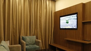 Ein Wohnzimmer mit Fernseher an einer Holzwand, einem Sofa, einem Sessel und einem Couchtisch.
