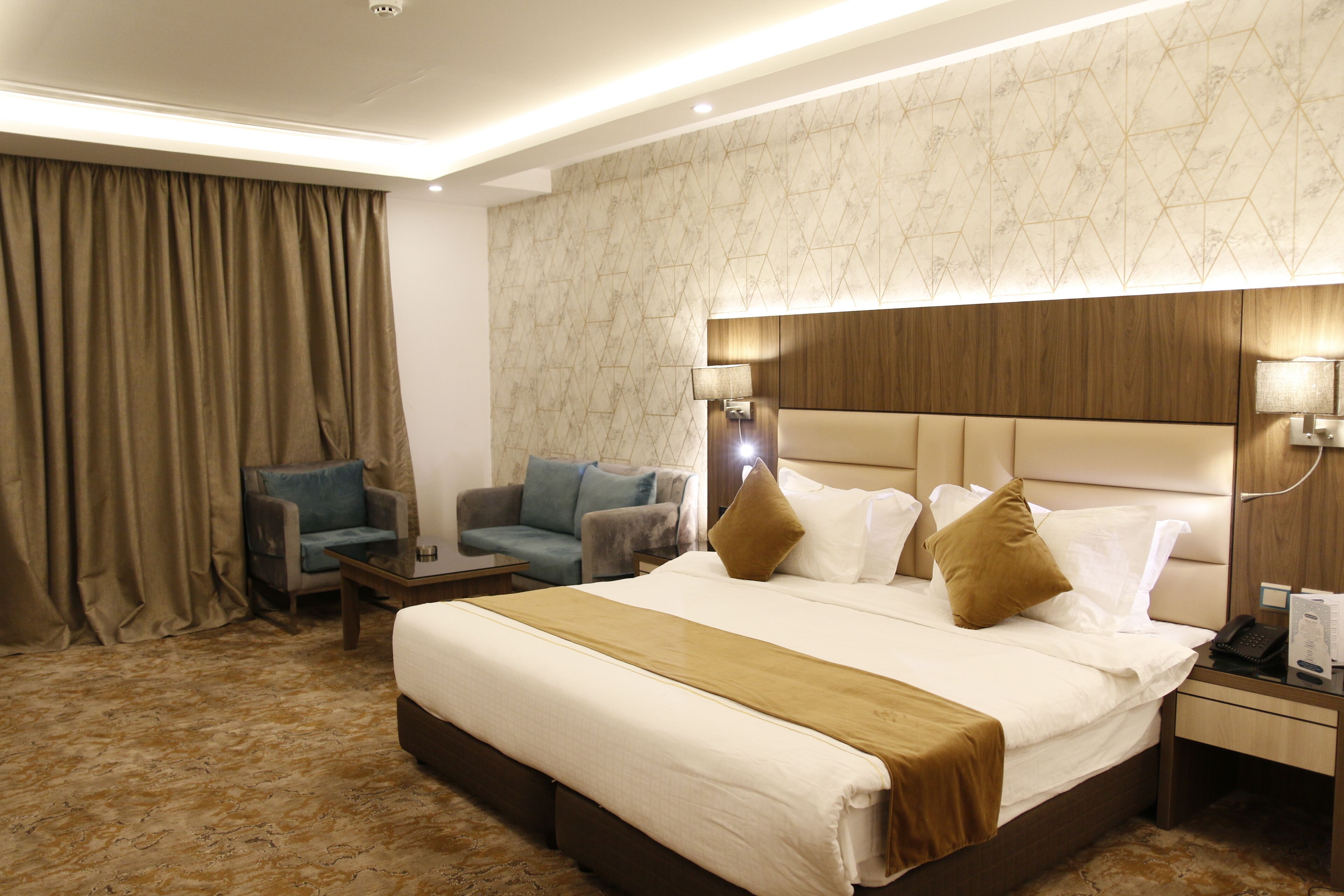 A hotel room with a large bed, a nightstand, a desk, two chairs, and a curtain.