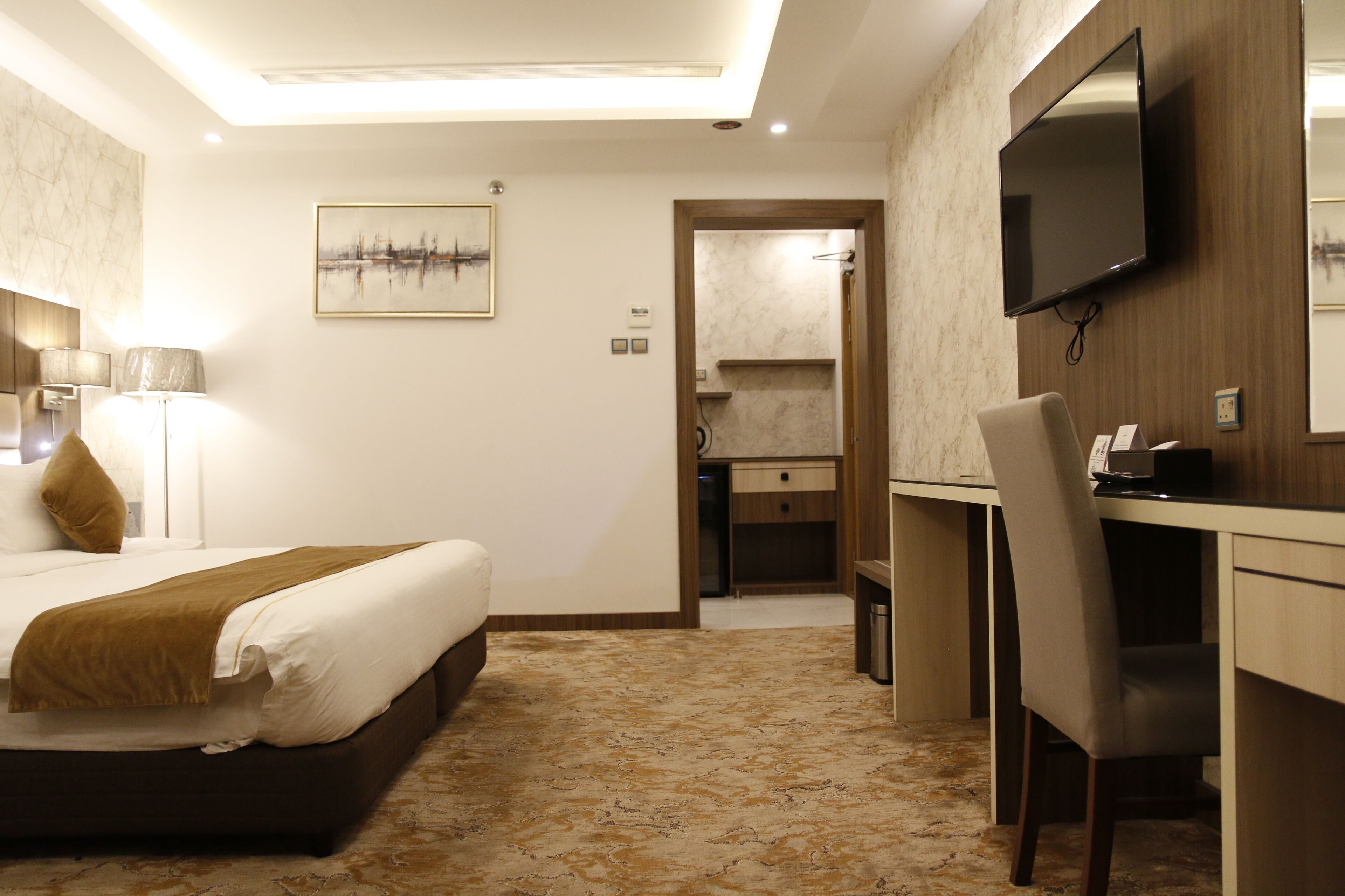 A hotel room with a bed, desk, chair, television, and artwork.
