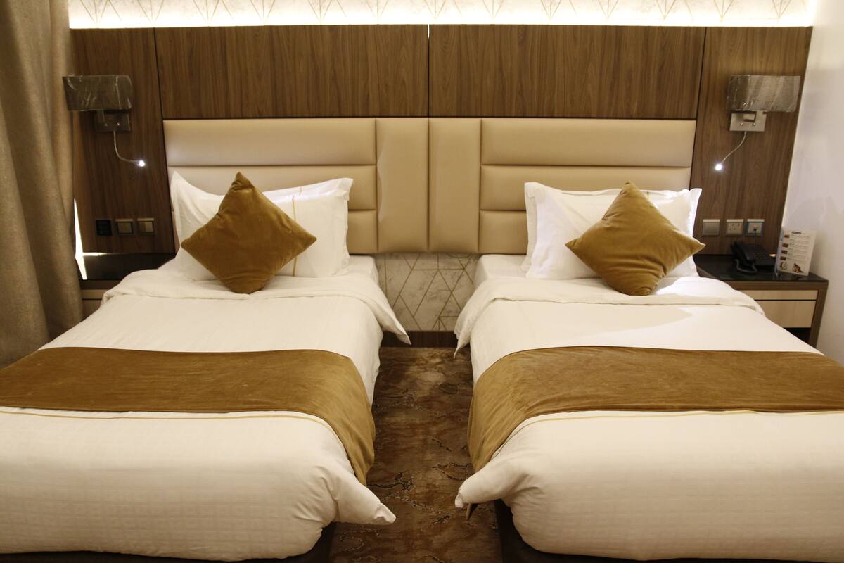 Ein Hotelzimmer mit zwei Betten, jeweils mit einer braunen Tagesdecke und einem Kopfkissen. Das Zimmer verfügt über hölzerne Kopfteile und Nachttische mit Lampen.