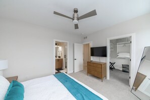 A bedroom with a bed, a ceiling fan, a TV, a wardrobe, and a walk-in closet.