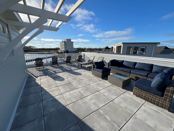 A rooftop patio with outdoor furniture, a white railing, and a view of the surrounding buildings.
