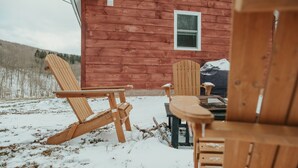 A wooden cabin with two Adirondack chairs and a table outside.