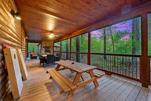 Une terrasse en bois avec des tables de pique-nique, un coin repas et une vue sur une forêt.
