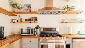 A modern kitchen with a stainless steel stove, a microwave, and a dishwasher. There are wooden shelves above the counter holding various kitchen items. - Family Friendly, Peaceful Yard, Dedicated Work Space, Close to Local Attractions (New Cumberland)