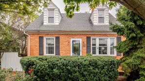 A two-story brick house with a well-maintained hedge in front, a white door, and a small garden with red flowers. - Family Friendly, Peaceful Yard, Dedicated Work Space, Close to Local Attractions (New Cumberland)