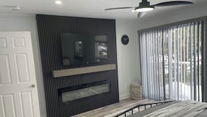A modern bedroom with a bed, a mounted TV, a ceiling fan, and a window with blinds. - Elegant waterfront retreat on Paudash Lake with sunset views! (Highlands east)