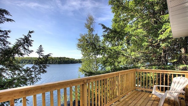A wooden deck with a view of a lake and trees. - Elegant waterfront retreat on Paudash Lake with sunset views! (Highlands east)