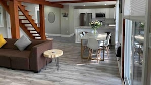 A spacious living area with a wooden staircase, a dining table with chairs, and a kitchen in the background. - Elegant waterfront retreat on Paudash Lake with sunset views! (Highlands east)