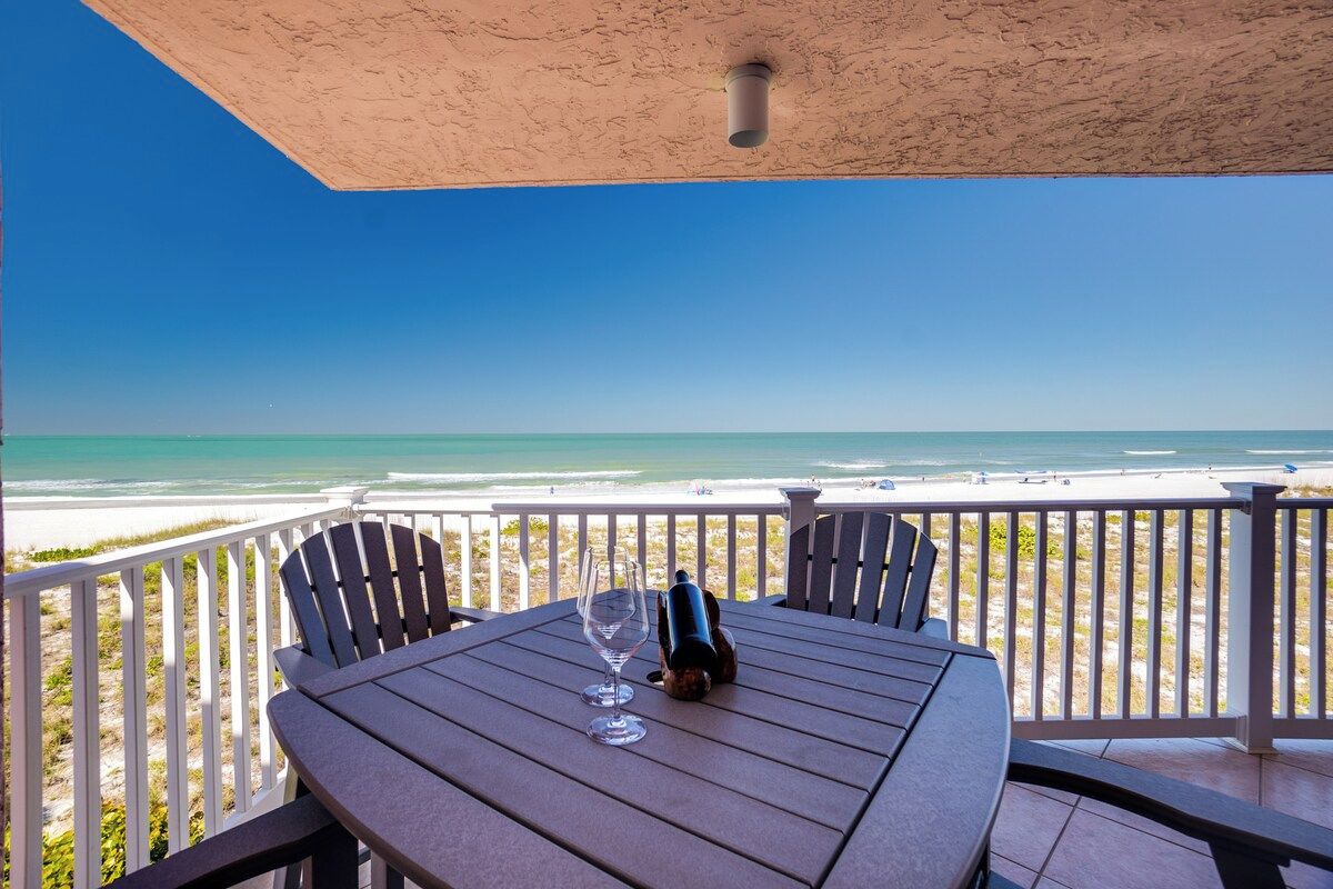 A table with a wine bottle and glass on a balcony overlooking a beach.