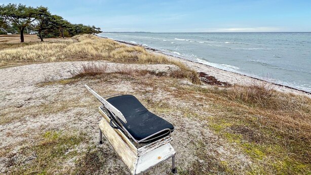 Una spiaggia con una panchina di legno e un oggetto nero sopra, con vista sull'oceano.