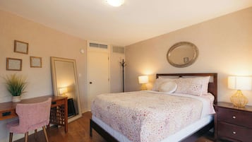 A bedroom with a bed, bedside lamps, a desk, a chair, a mirror, and a potted plant.