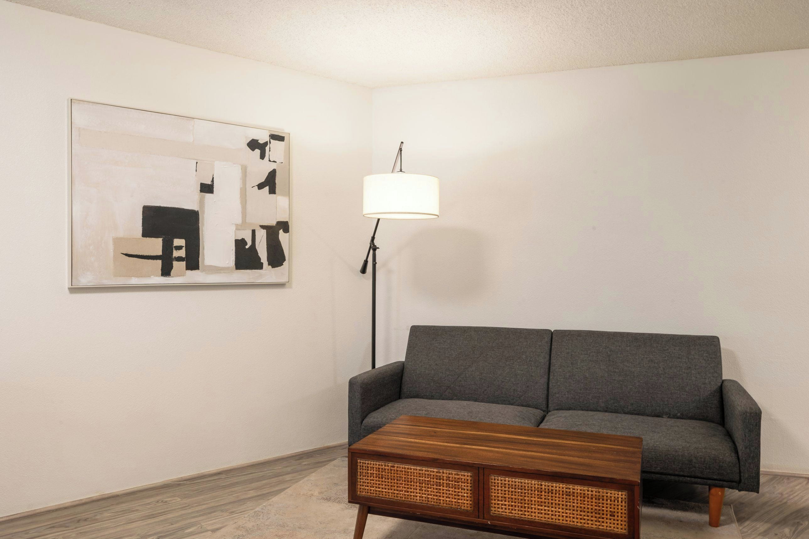 A living room with a grey sofa, a wooden coffee table, a floor lamp, and a piece of abstract art on the wall.