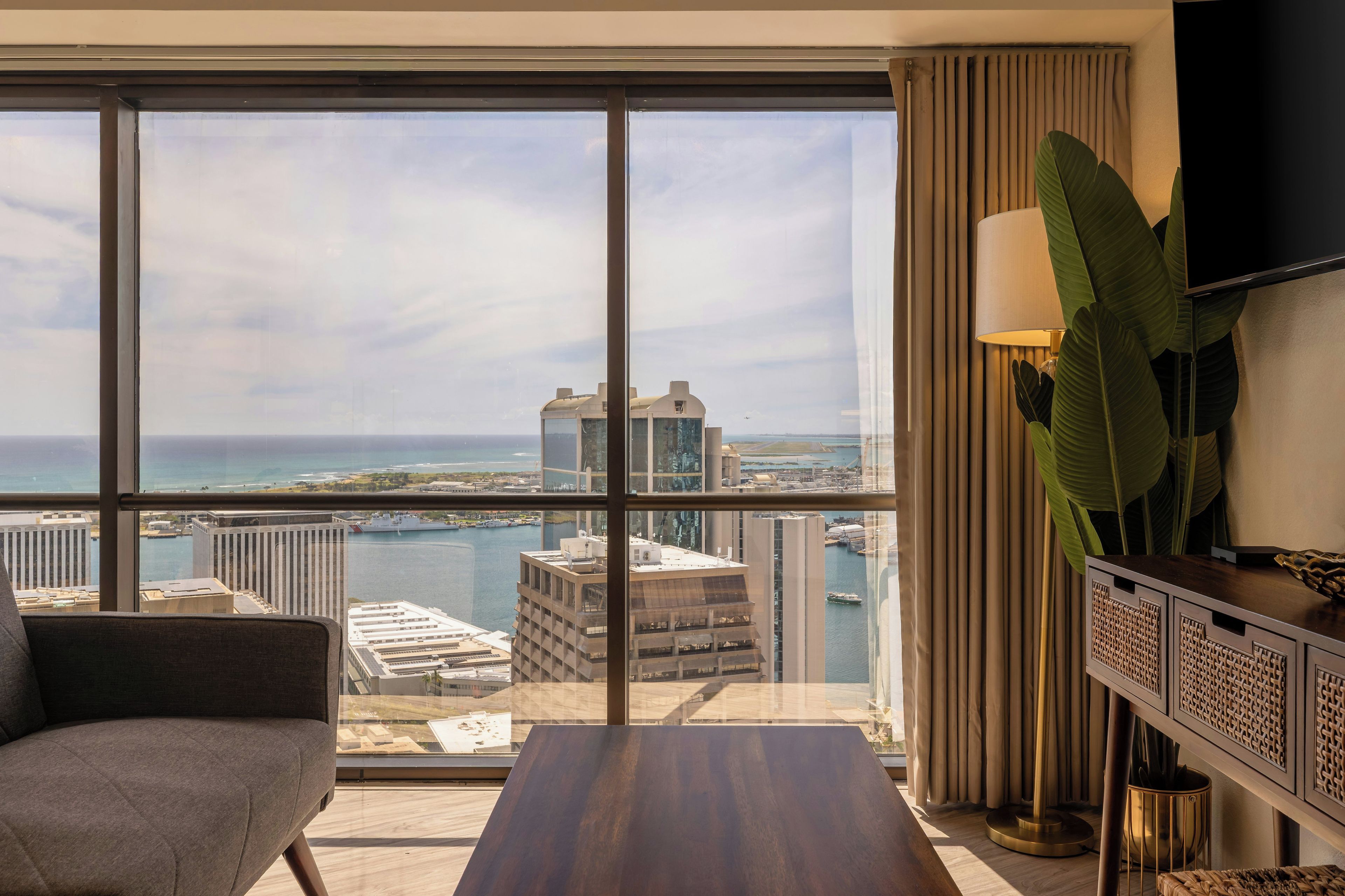 Una habitación de hotel moderna con un ventanal grande que ofrece vistas a la ciudad y al mar.