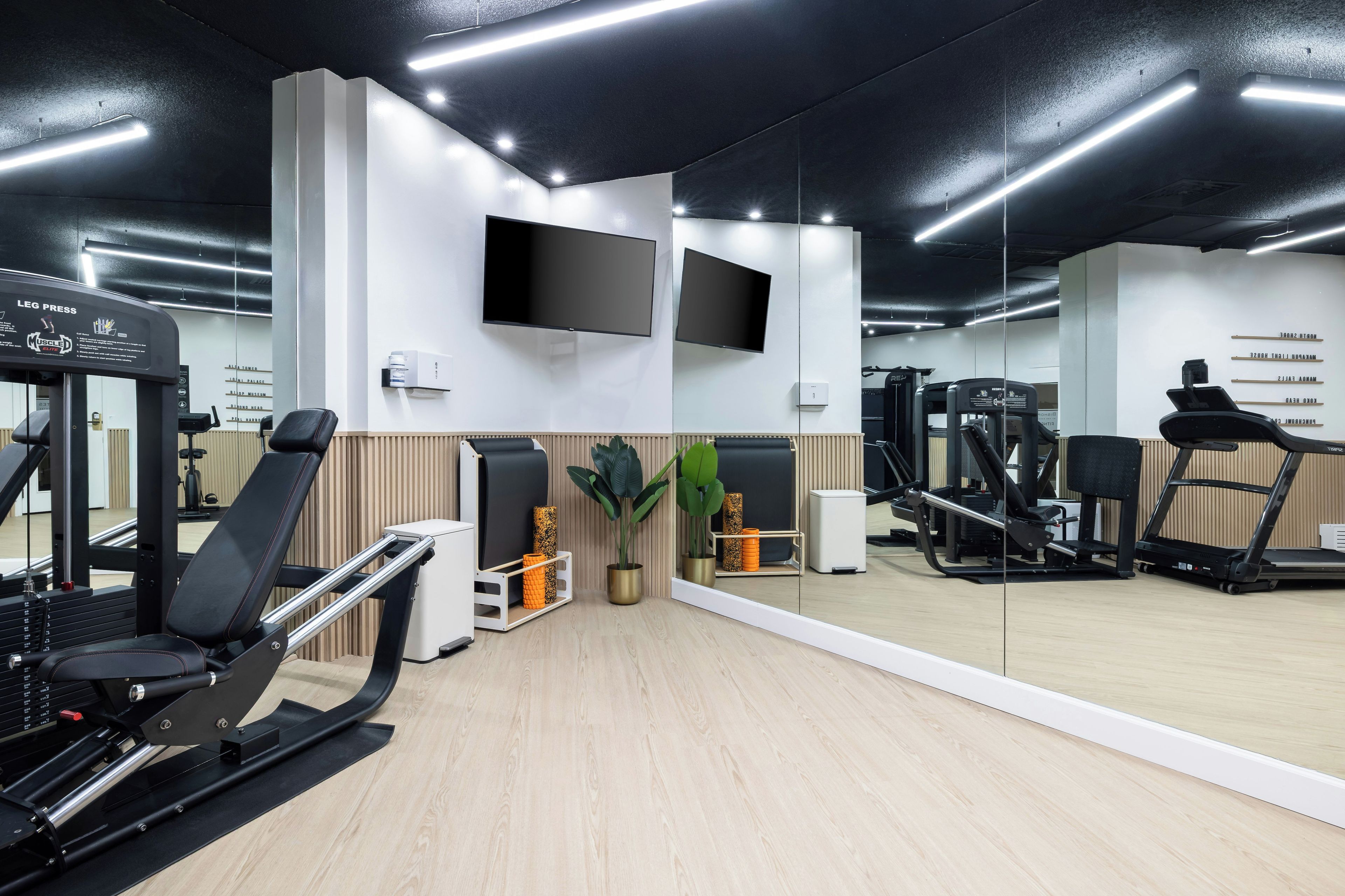 Un gimnasio con equipo de ejercicio, un televisor montado en la pared y un espejo que refleja el espacio.