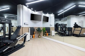 A gym with exercise equipment, a TV mounted on the wall, and a mirror reflecting the space. - Bishop Suites Downtown Honolulu (Honolulu)