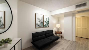 A modern interior with a black sofa, a round mirror, and two framed botanical prints on the wall.