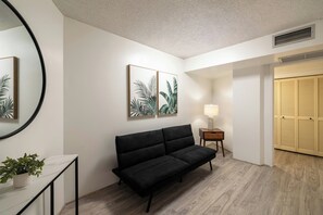 A modern interior with a black sofa, a round mirror, and two framed botanical prints on the wall. - Bishop Suites Downtown Honolulu (Honolulu)