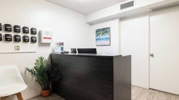 A reception desk with a computer, a plant, and a painting of palm trees.