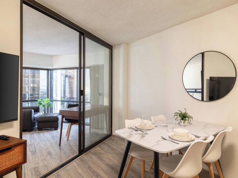 A modern dining area with a glass partition, a round mirror, and a dining table set for two.