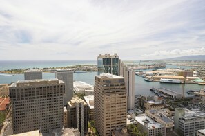 A high-rise building with a modern glass facade, surrounded by other commercial buildings, a marina with boats, and a clear view of the coastline. - Bishop Suites Downtown Honolulu (Honolulu)