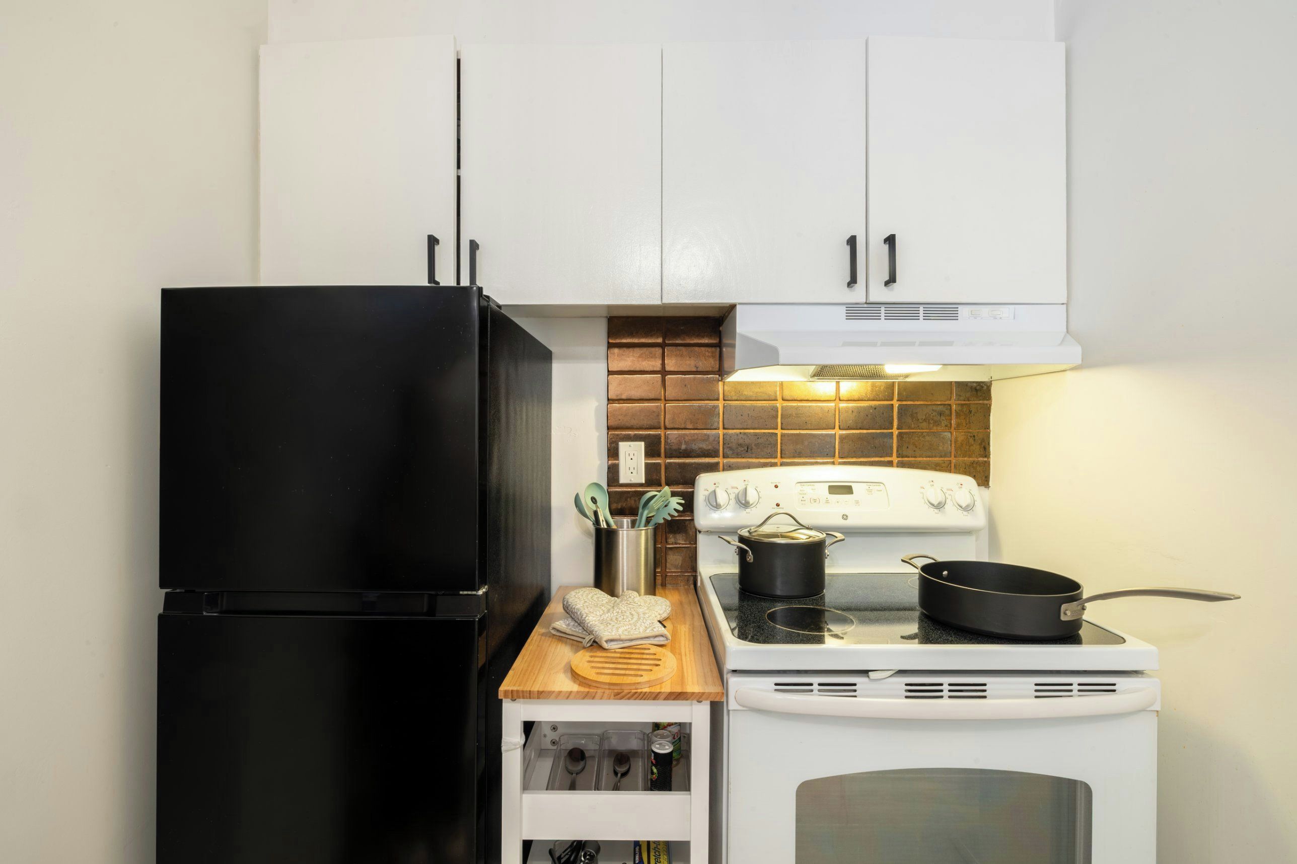A kitchen with white cabinets, a black refrigerator, a white stove, and a wooden countertop.