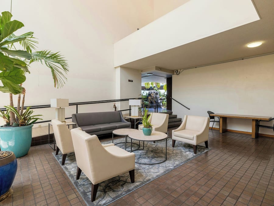 A spacious lobby with a grey sofa, two armchairs, a small round table, and a potted plant.