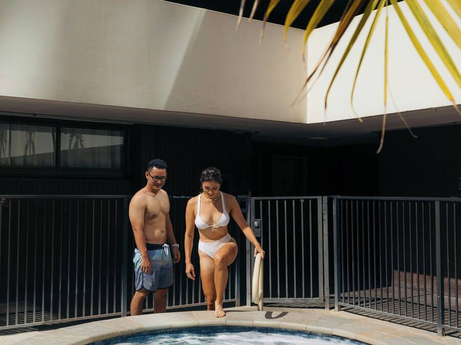 A hot tub with a stone border, a metal fence, and a building with a balcony in the background.