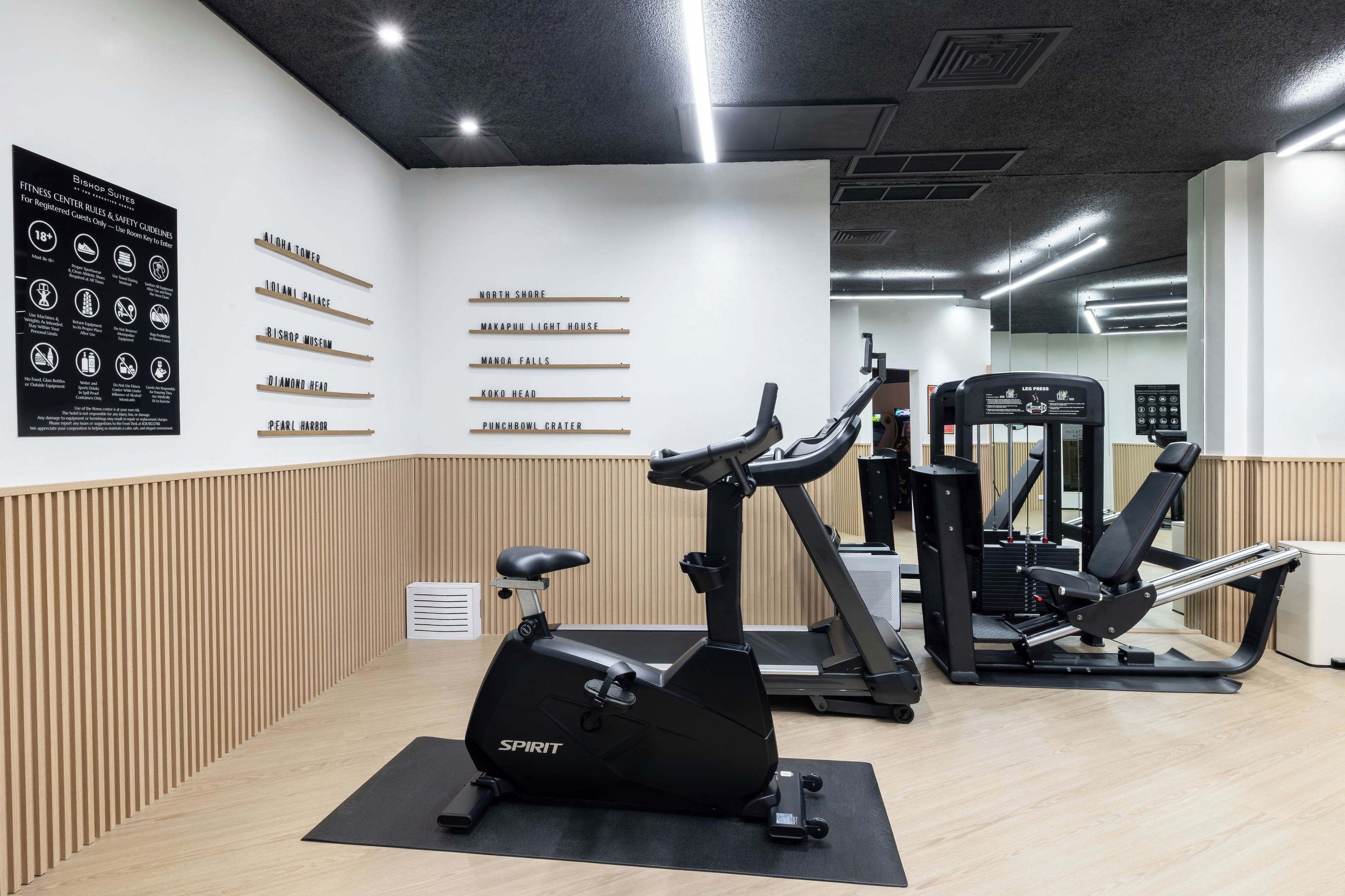 Un gimnasio con máquinas de cardio, equipo de entrenamiento de pesas y una pared con pautas de seguridad.